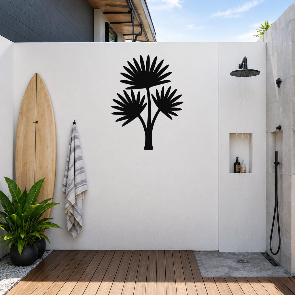 Black metal cutout palm tree wall art with three fan-shaped fronds, mounted on a white outdoor wall above a wooden deck near a shower area.