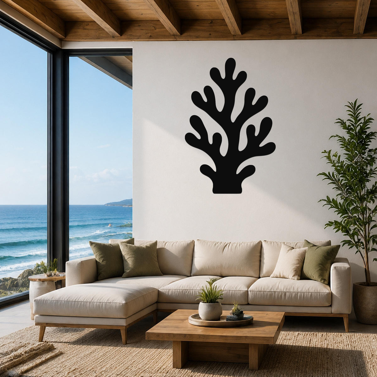 Black metal coral wall art with branching cutouts, mounted on a white wall above a beige sectional sofa in a coastal living room with ocean views.