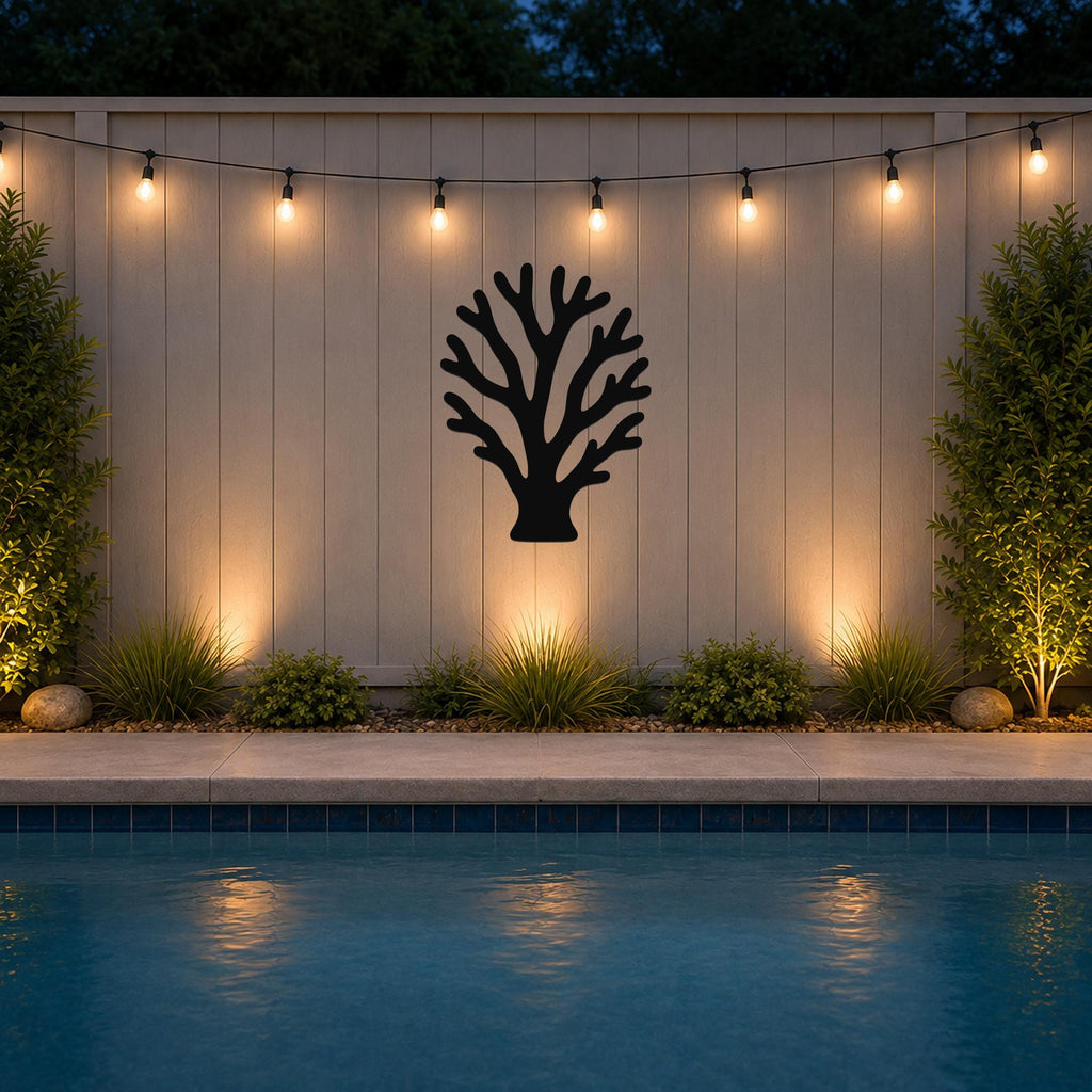 Black metal branching coral wall art with intricate cutout details, mounted on a light-colored outdoor wall above a poolside garden.