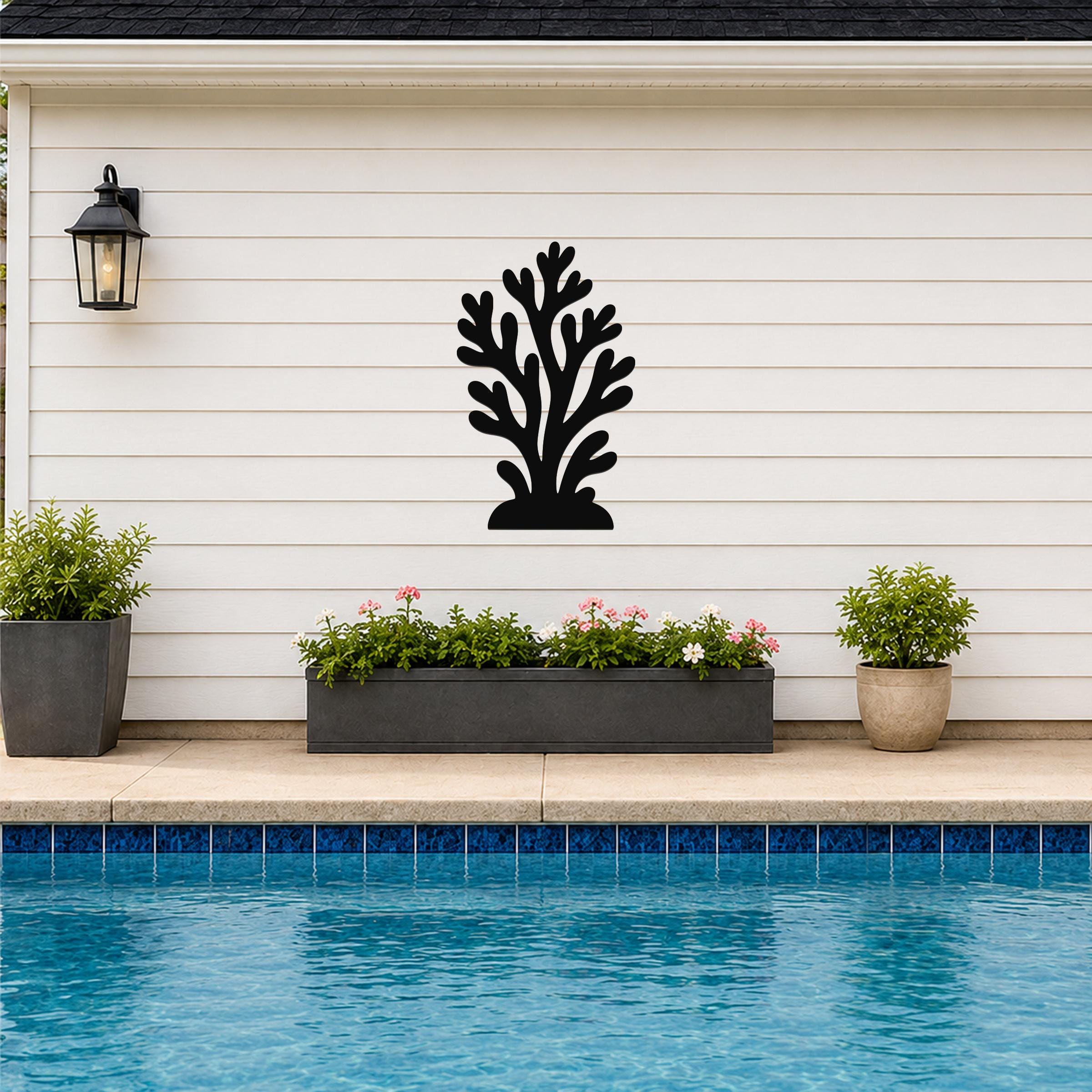Black metal coral wall art with branching cutouts, mounted on a white horizontal siding wall above a poolside planter.