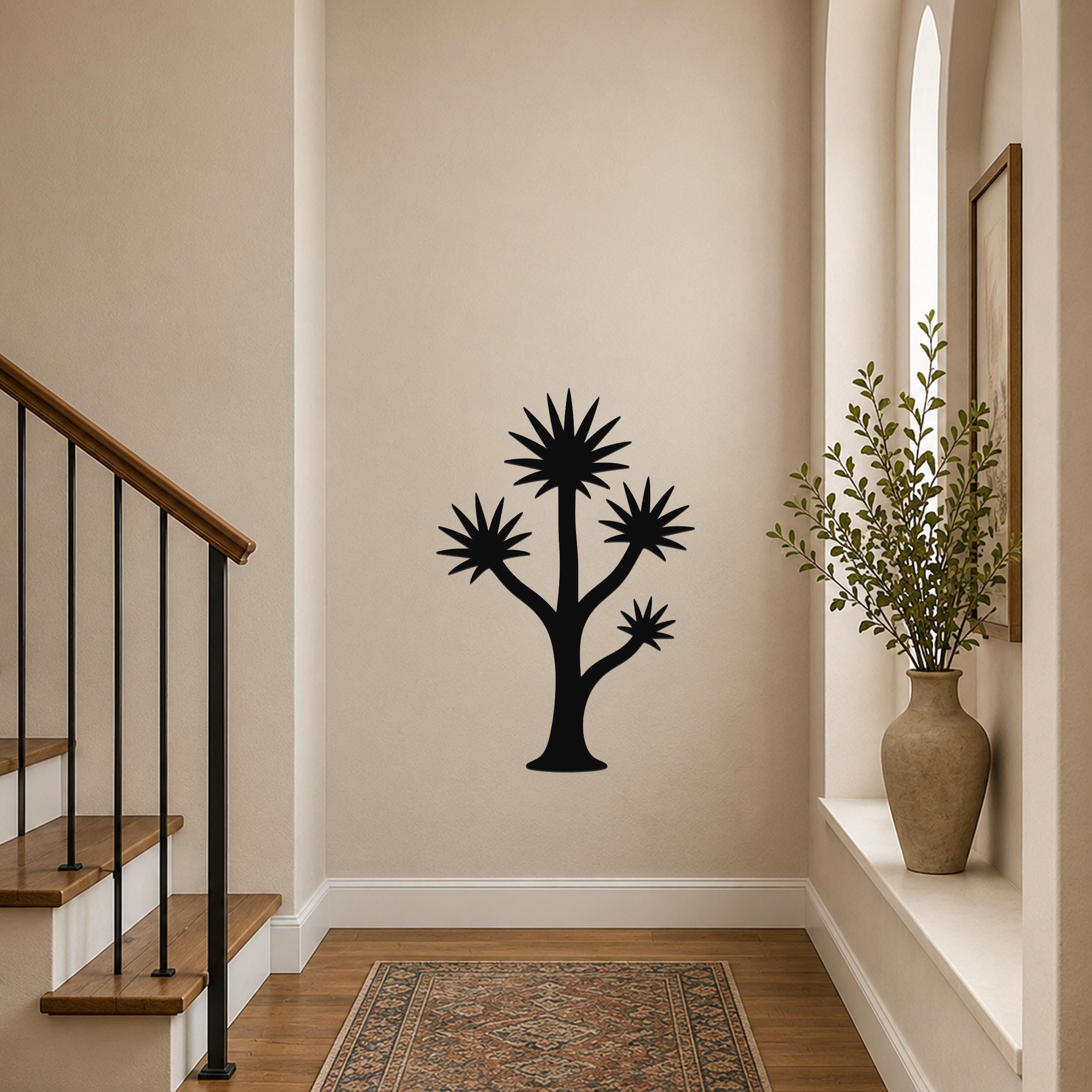 Black metal wall art in a tall yucca silhouette with starburst-shaped leaves, mounted on a hallway wall above a patterned rug.
