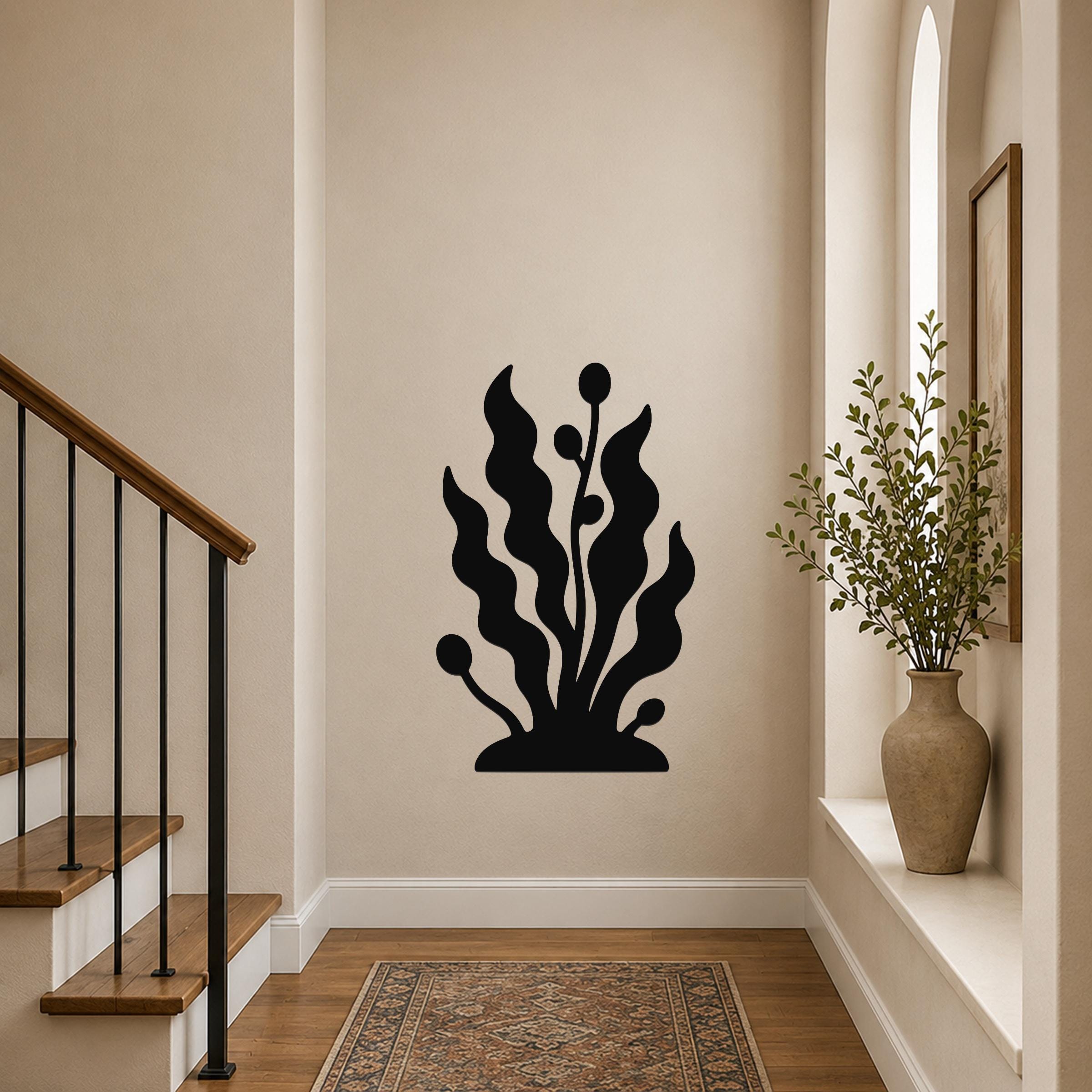 Black metal wall art in a kelp and seaweed silhouette design, mounted on a hallway wall above a patterned rug near a staircase.