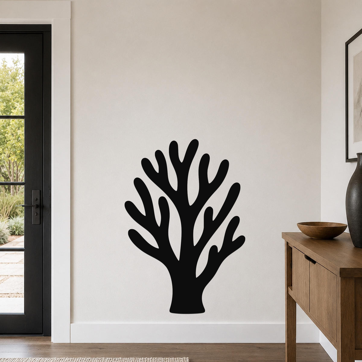 Black metal coral wall art with branching cutouts, mounted on a light-colored wall in a modern entryway.