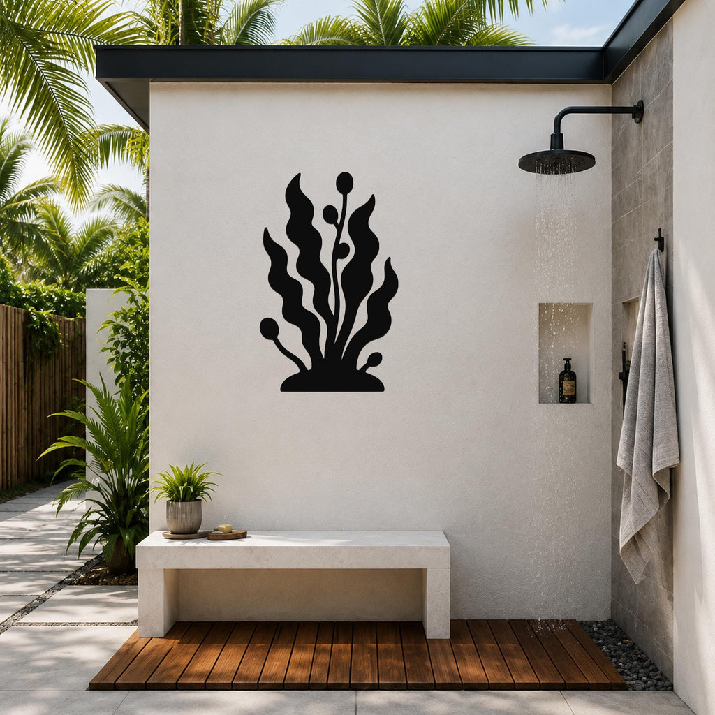 Black metal kelp and seaweed wall art silhouette mounted on a white outdoor shower wall, above a concrete bench in a tropical patio setting.