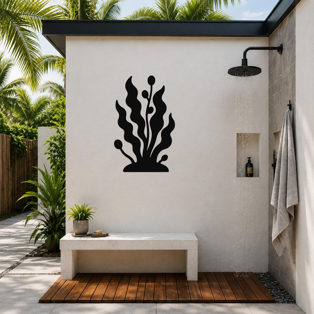 Black metal kelp and seaweed wall art silhouette mounted on a white outdoor shower wall, above a concrete bench in a tropical patio setting.