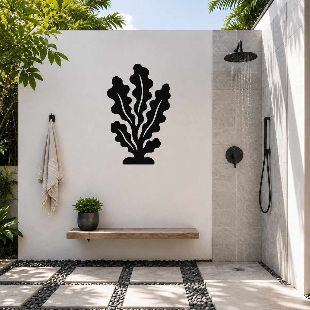 Black metal kelp wall art with leafy cutout design, mounted on a white outdoor wall above a wooden bench in a modern shower area.