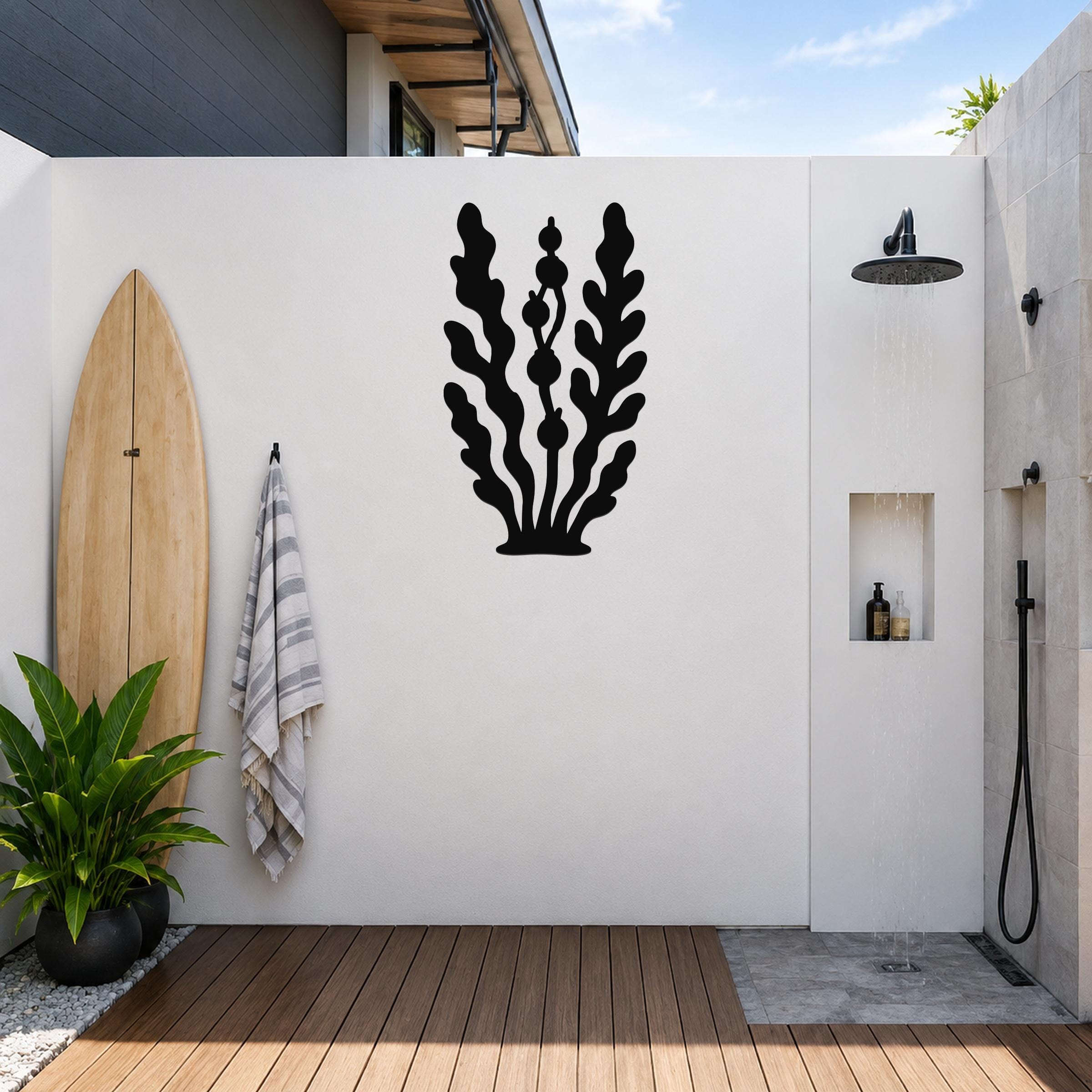 Black metal kelp and seaweed wall art with leafy cutouts, mounted on a white outdoor wall above a wooden deck near a shower area.