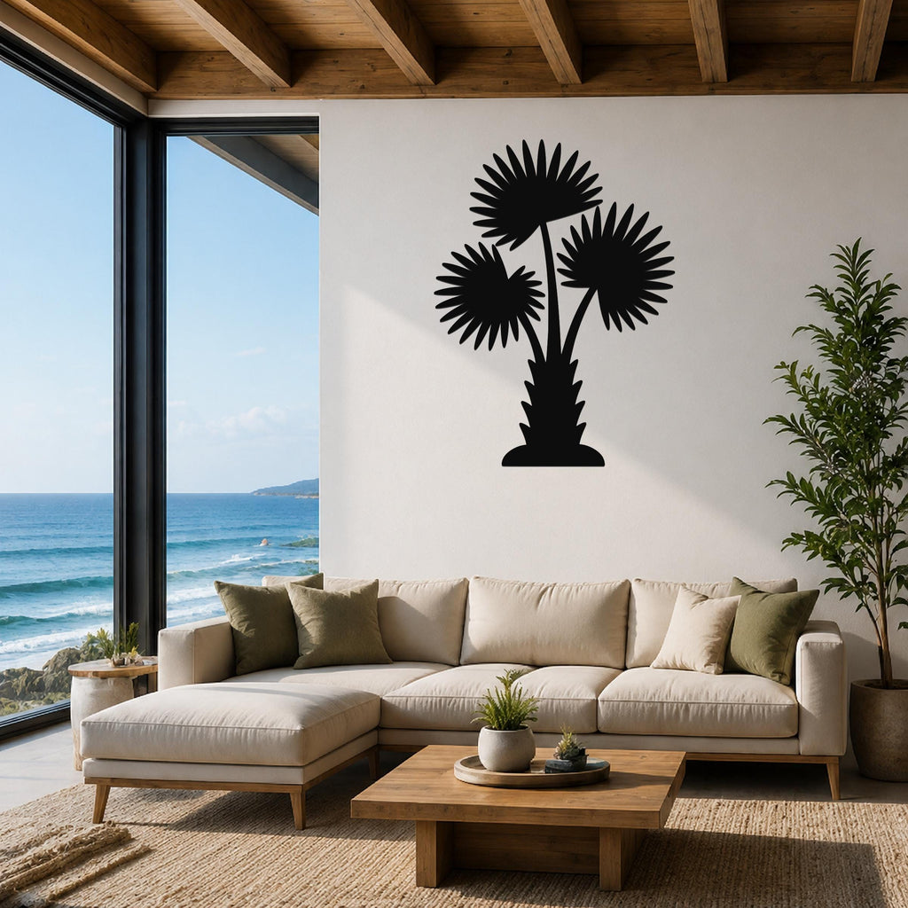 Black metal wall art of a fan palm tree silhouette with three fronds, mounted on a white wall above a beige sectional sofa in a living room with ocean views.