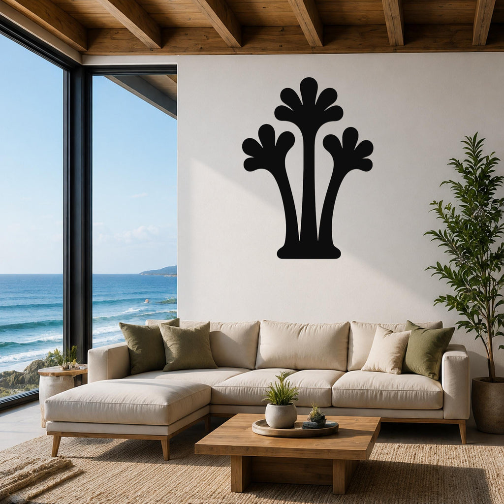 Black metal palm tree wall art with three fronded silhouettes, mounted on a white wall above a beige sectional sofa in a coastal living room.