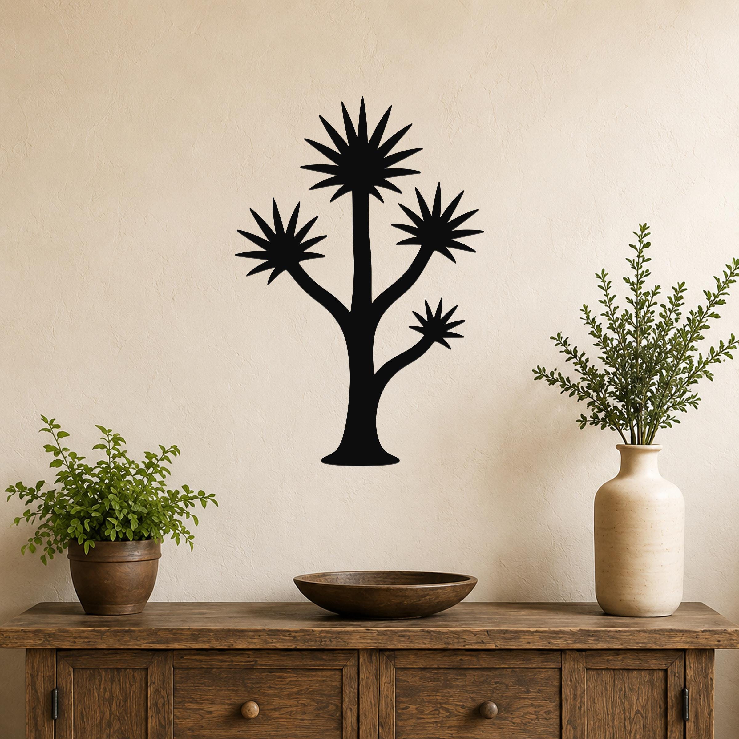 Black metal yucca wall art with starburst leaves and branching silhouette, mounted on a beige wall above a wooden console table.
