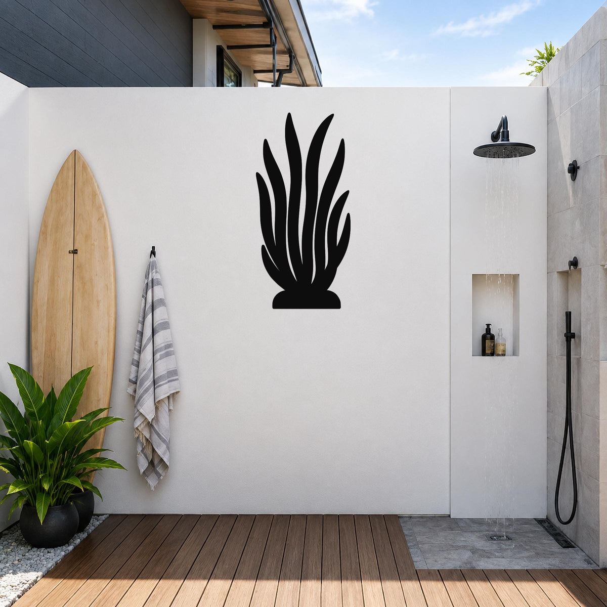 Black metal kelp wall art silhouette mounted on a white outdoor wall beside a shower, with a surfboard and potted plant nearby.