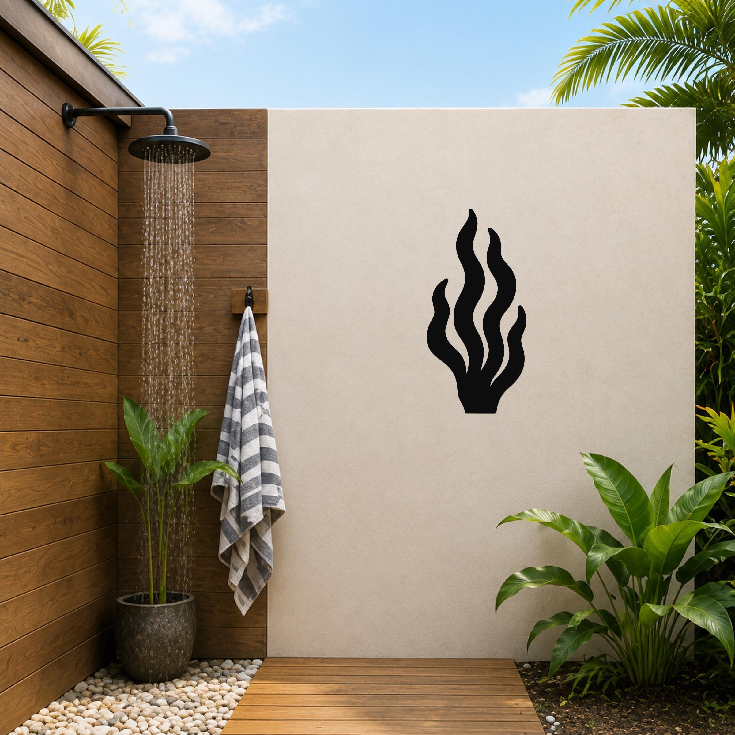 Black metal kelp wall art with flowing seaweed cutouts, mounted on a beige outdoor wall beside a wooden shower area.