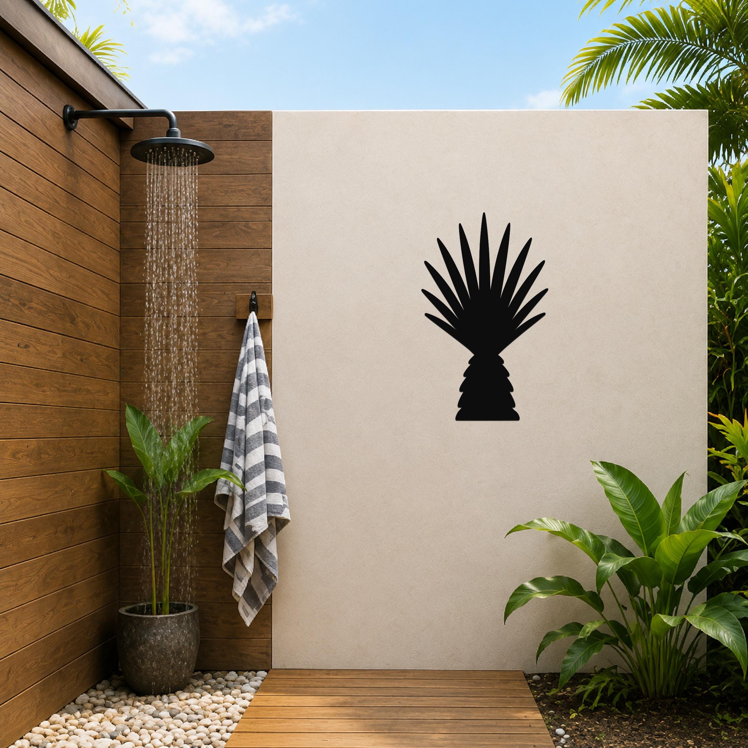 Black metal palm tree wall art with fan-shaped fronds, mounted on a beige outdoor wall beside a wooden shower area.