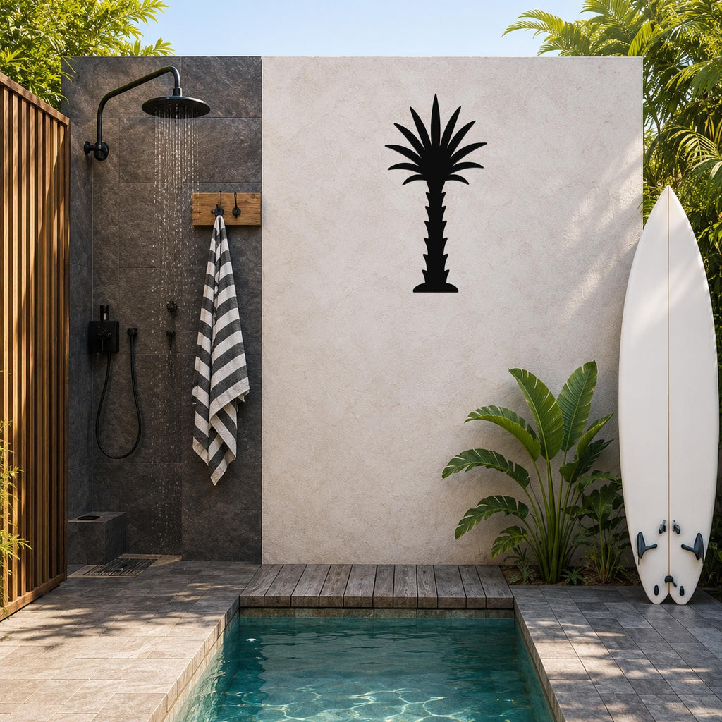 Black metal palm tree wall art silhouette mounted on a light-colored outdoor wall beside a shower and pool area.
