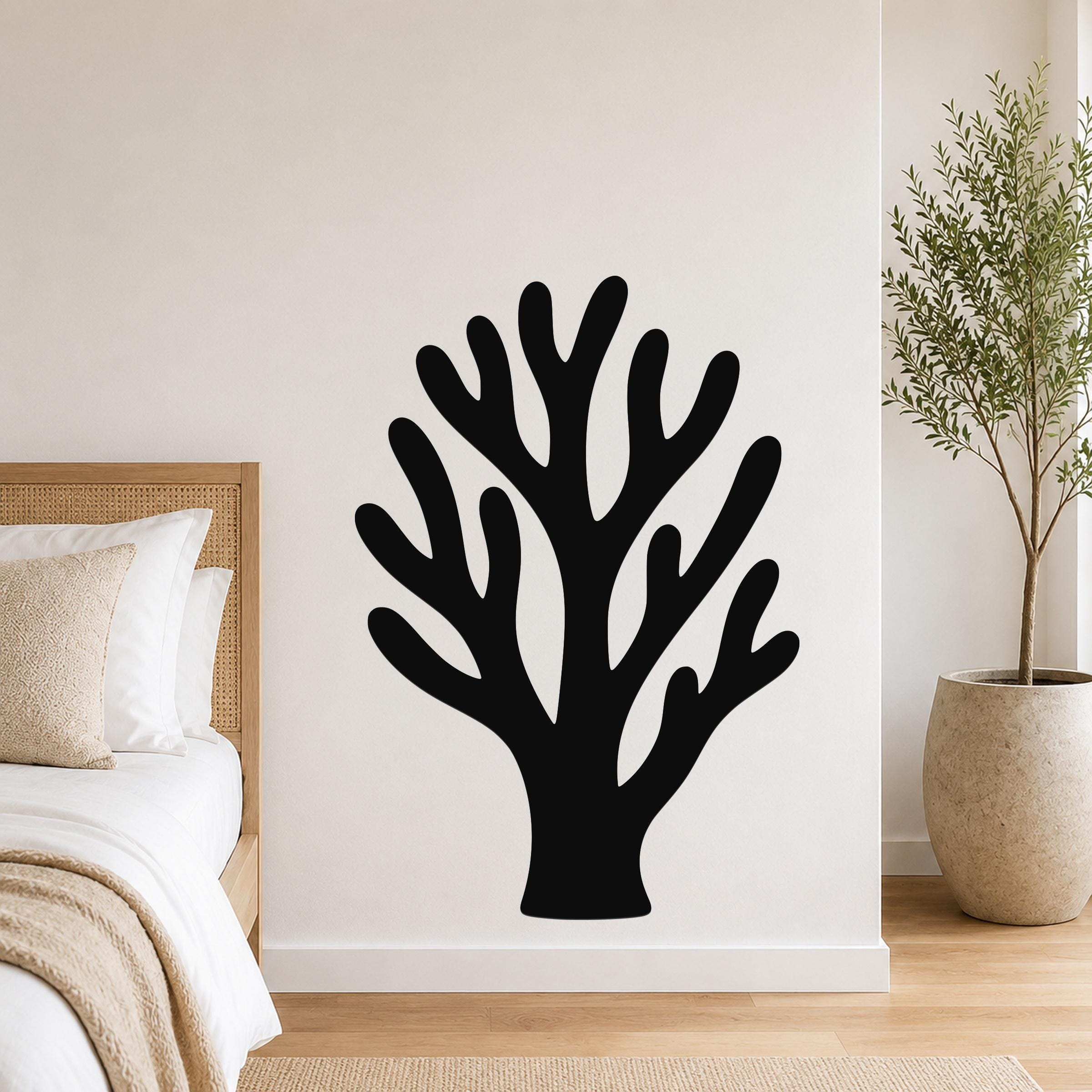 Black metal coral wall art with branching cutouts, mounted on a white bedroom wall above a bed.