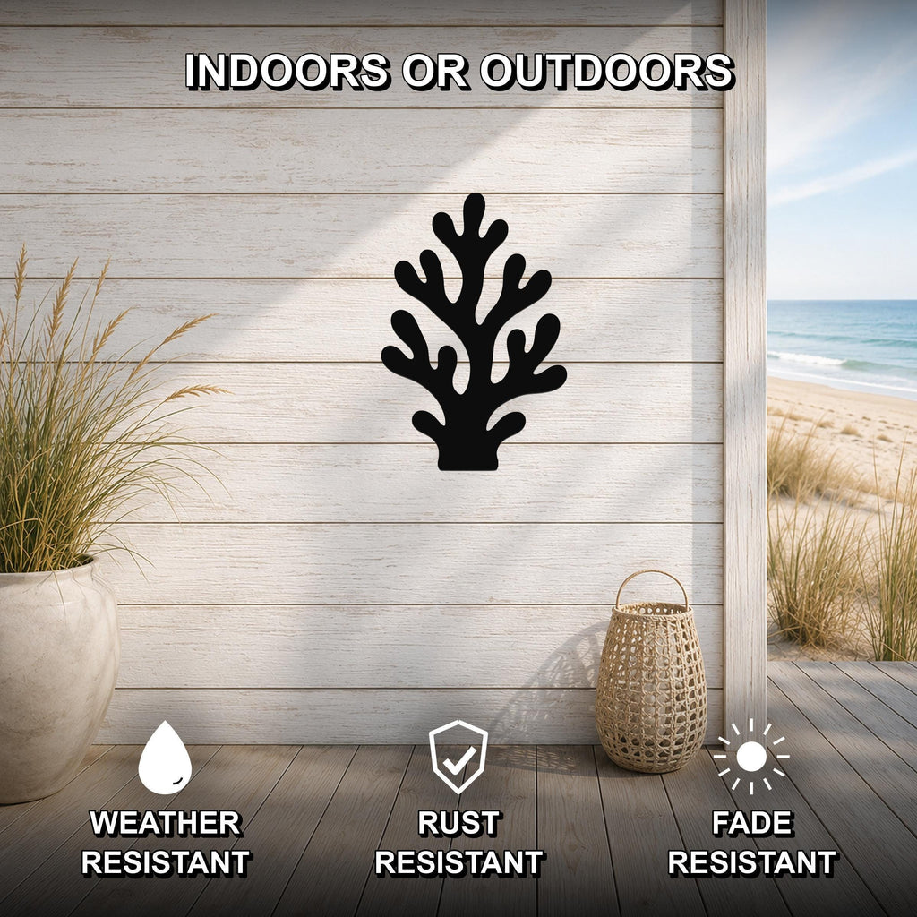 Black metal coral wall art with branching cutouts, mounted on a light wood plank wall above a wooden deck with a beach view.