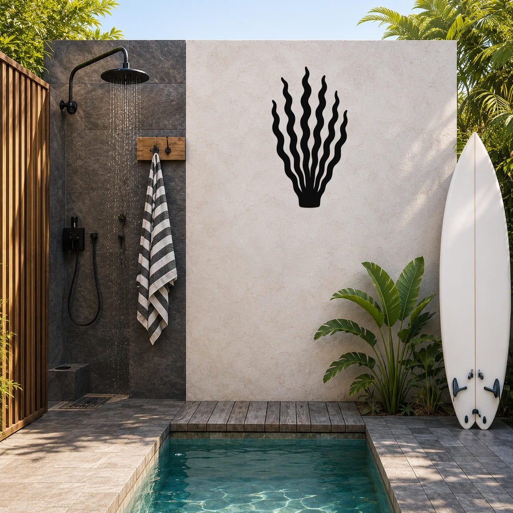 Black metal kelp wall art with wavy frond cutouts, mounted on a light-colored outdoor wall beside a shower and pool area.