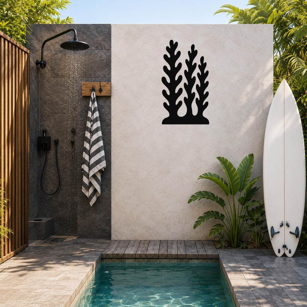Black metal wall art with a kelp and seaweed silhouette design, mounted on a light-colored outdoor wall beside a shower and pool area.