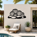 Black metal barrel cactus wall art with detailed spine cutouts, mounted on a white outdoor wall above a lounge chair near a pool.