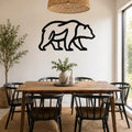 Black metal bear silhouette wall art mounted on a white wall above a wooden dining table in a bright, modern dining room.