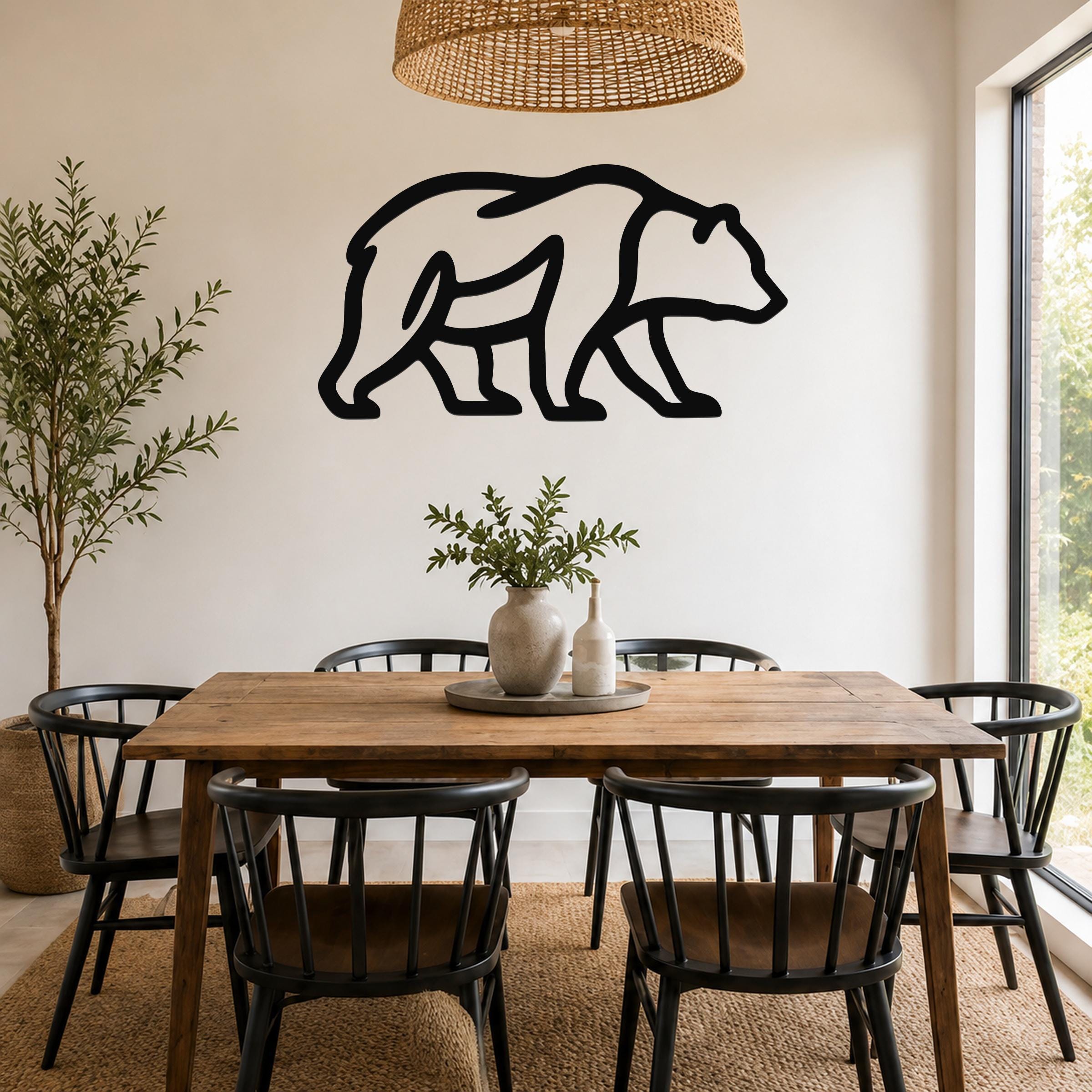 Black metal bear silhouette wall art mounted on a white wall above a wooden dining table in a bright, modern dining room.