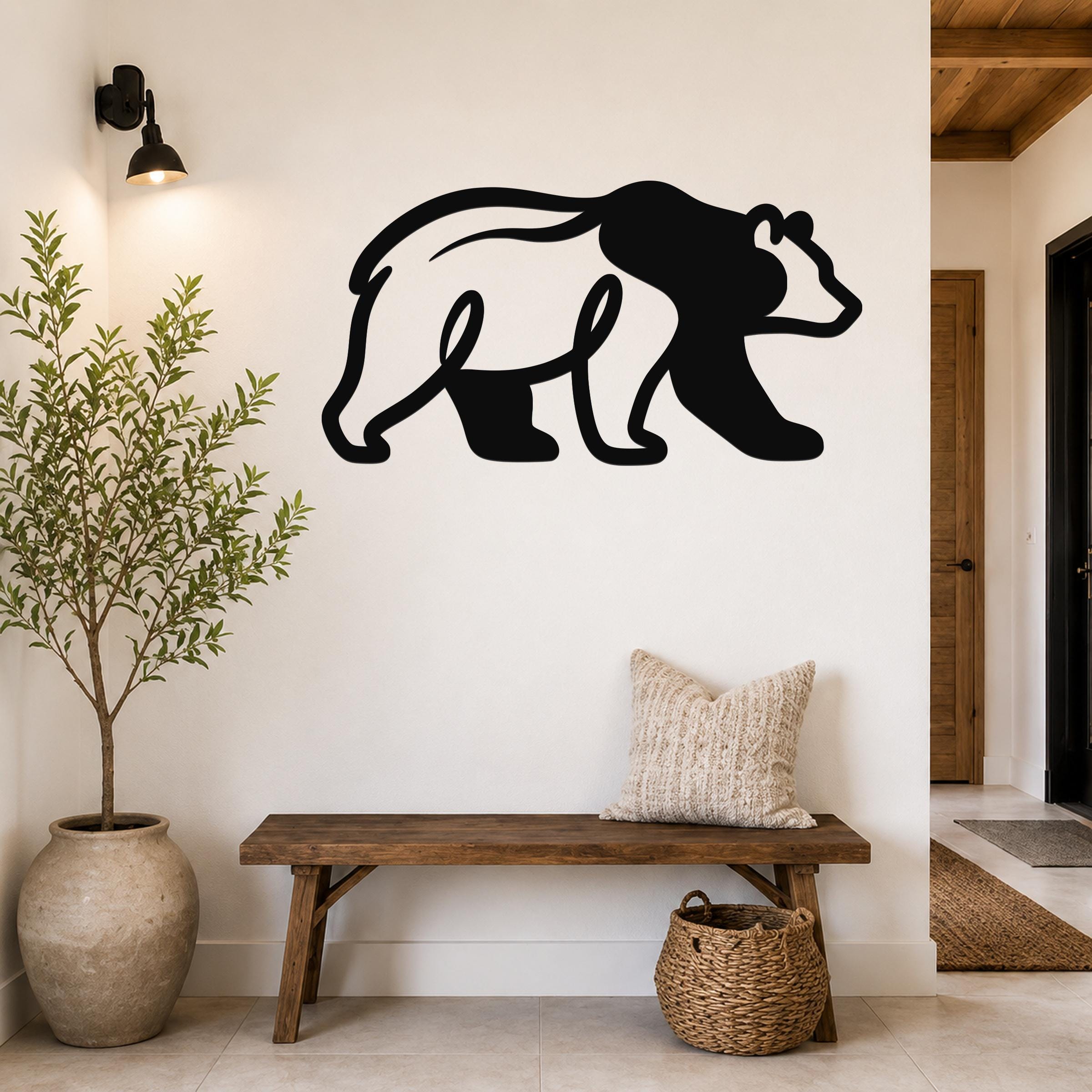 Black metal bear wall art silhouette mounted on a white wall above a wooden bench in a rustic entryway.