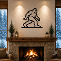 Black metal Bigfoot wall art silhouette mounted above a stone fireplace in a cozy living room with snow outside.