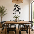 Black metal Bigfoot silhouette wall art mounted on a white wall above a wooden dining table in a bright, modern dining room.