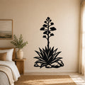 Black metal agave wall art with a blooming flower silhouette, mounted on a bedroom wall above a bed.