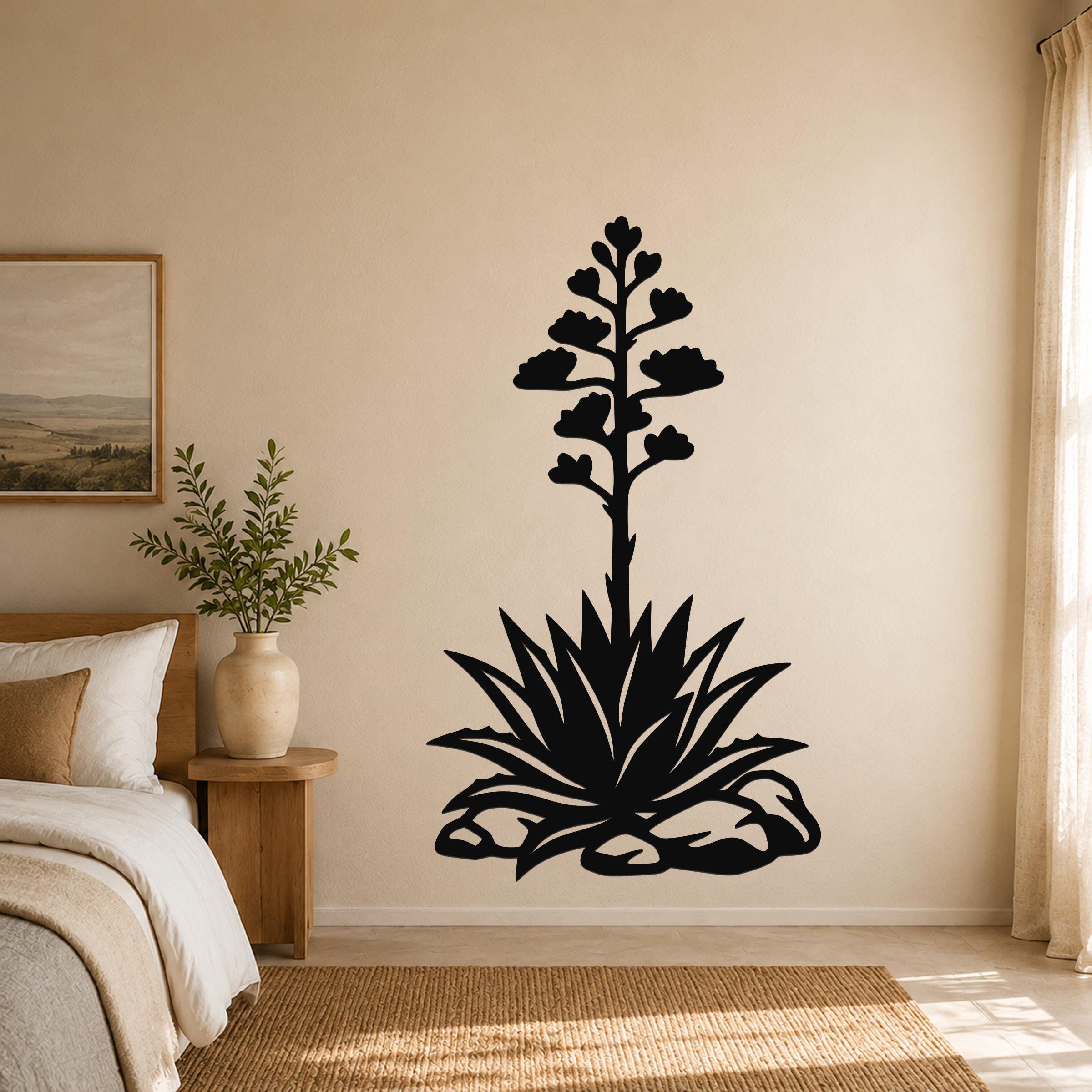 Black metal agave wall art with a blooming flower silhouette, mounted on a bedroom wall above a bed.