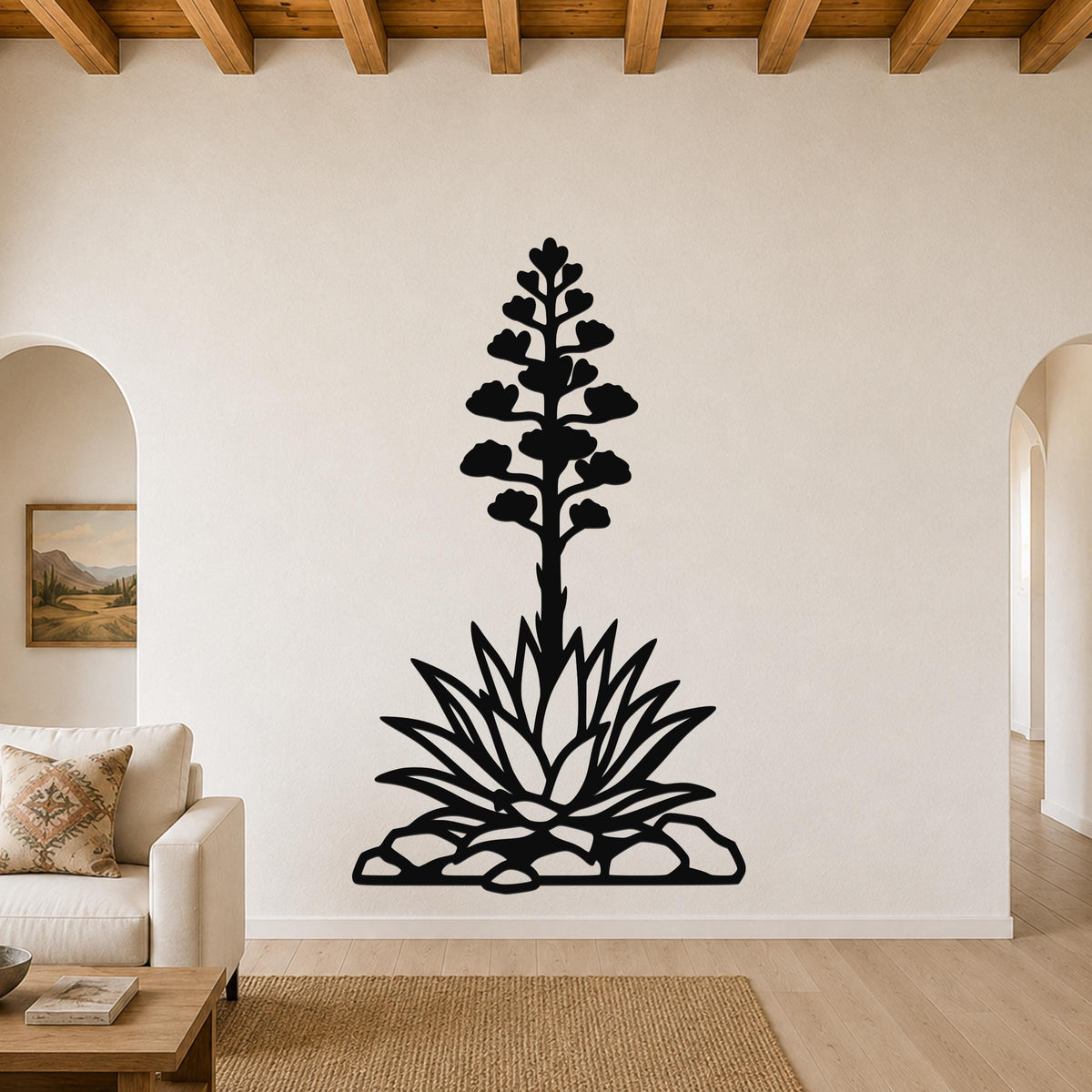 Black metal wall art in the silhouette of a blooming agave plant with a tall flower stalk and spiky leaves, mounted on a living room wall above a sofa.