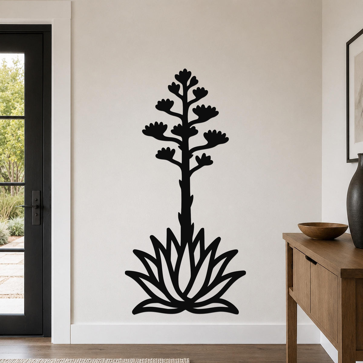 Black metal agave wall art with a blooming flower stalk and rosette cutouts, mounted on a light-colored wall in a living room.