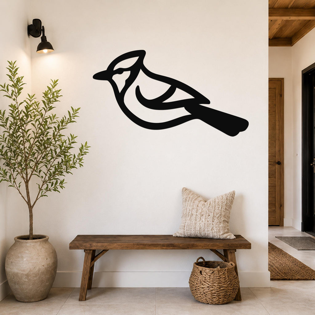 Black metal blue jay wall art silhouette mounted on a white wall above a wooden bench in a entryway.