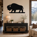 Black metal bison silhouette wall art mounted above a dark wood console table in a living room with a snowy mountain view.