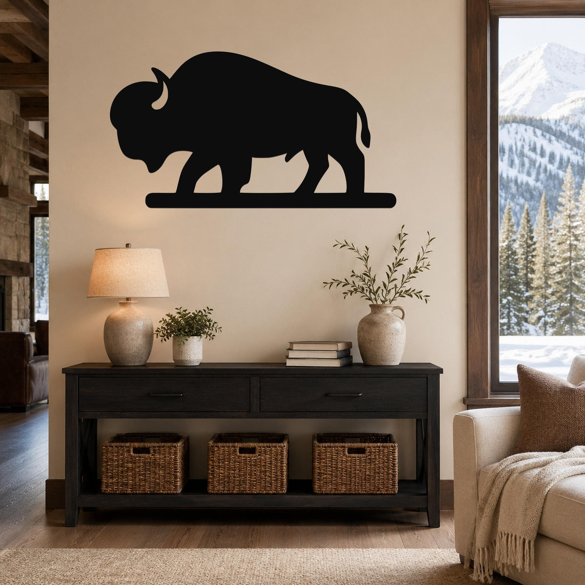 Black metal bison silhouette wall art mounted above a dark wood console table in a living room with a snowy mountain view.