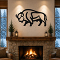 Black metal bison silhouette wall art mounted above a stone fireplace in a rustic living room with a snowy forest view.
