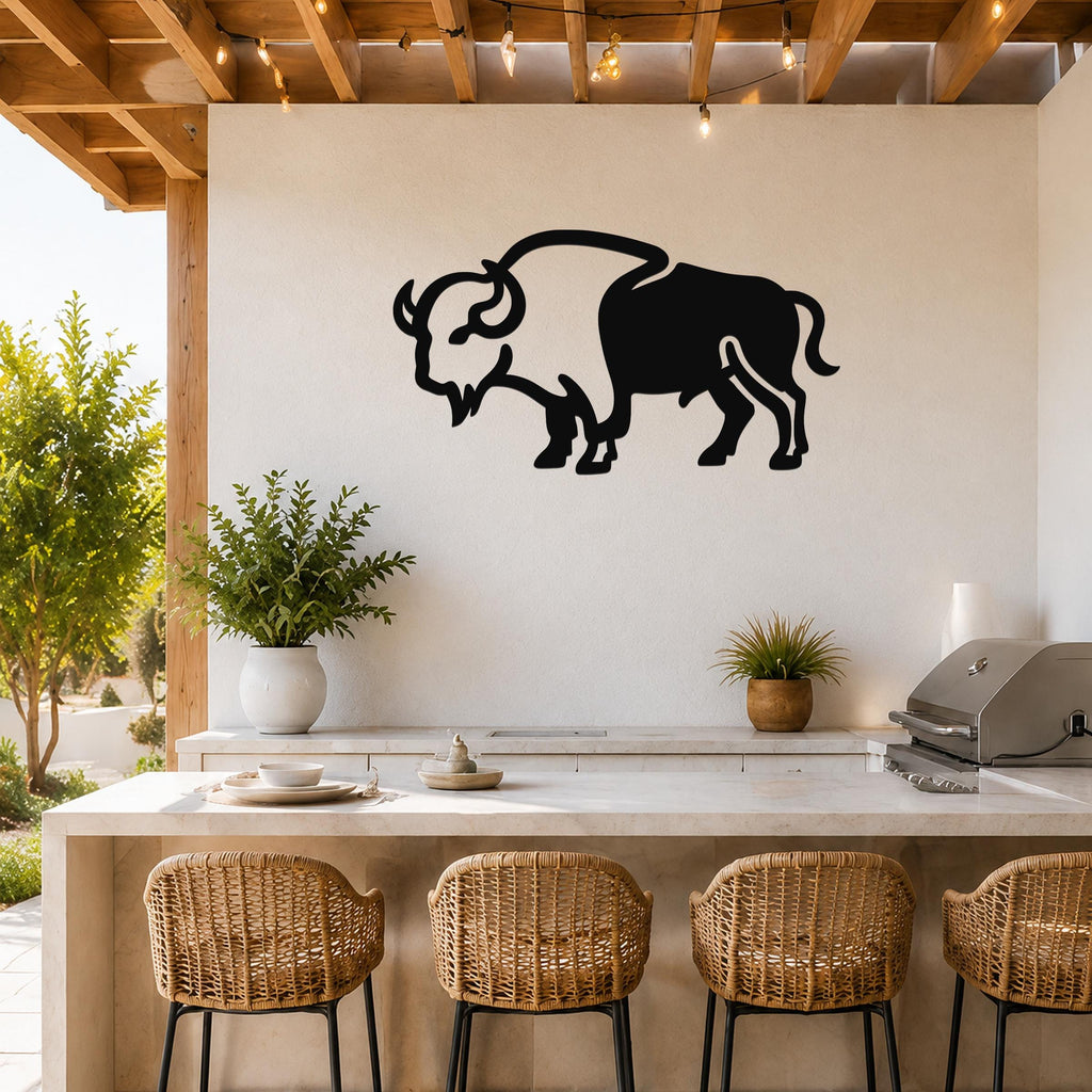 Black metal buffalo silhouette wall art mounted on a white wall above a kitchen counter in a covered outdoor patio with string lights and wicker bar stools.