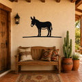 Black metal donkey wall art silhouette mounted on a stucco wall above a wooden bench in a sunlit patio entryway.