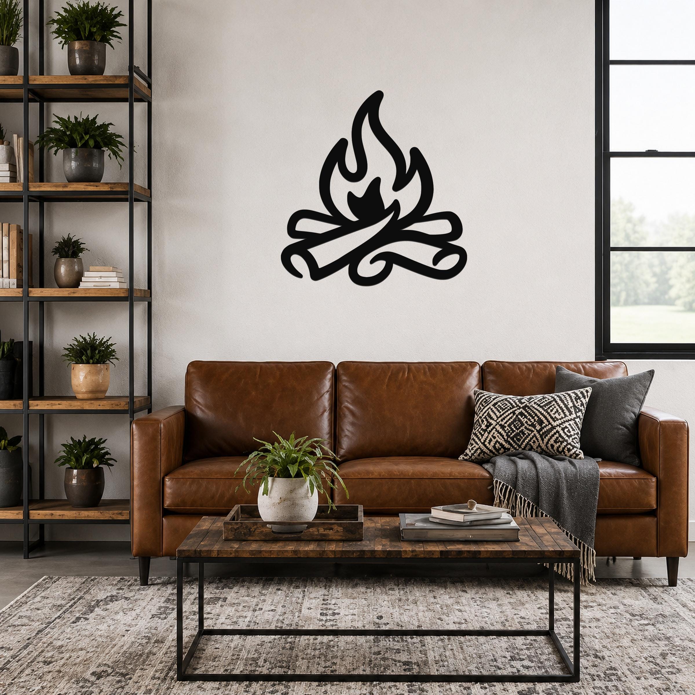 Black metal campfire wall art with flame and log silhouette, mounted above a brown leather sofa in a living room.