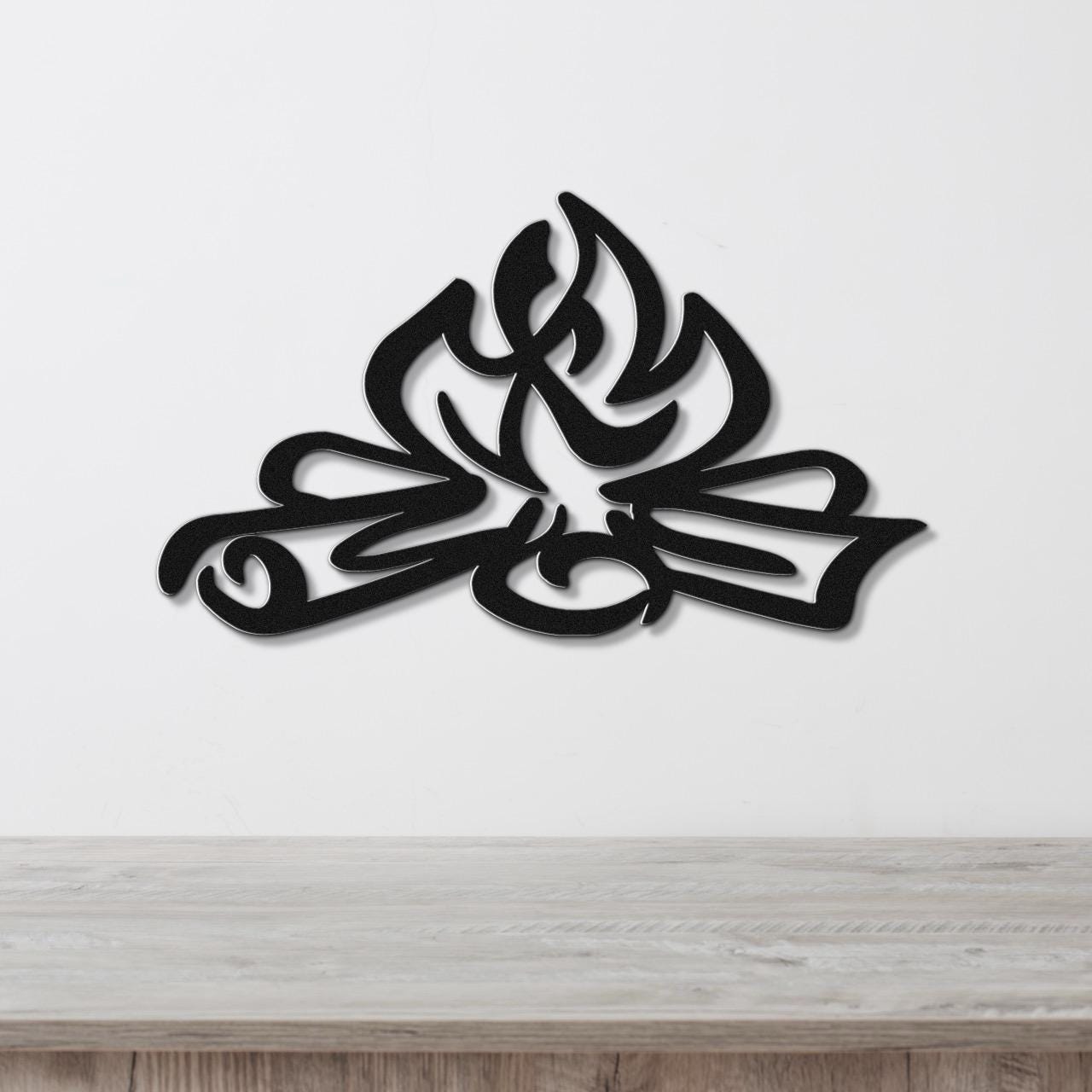 Black metal wall art with a flame and leaf cutout design, mounted on a white wall above a light wood counter.