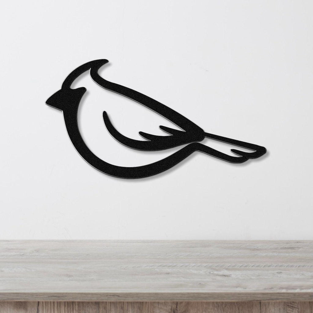 Black metal cardinal wall art with a bold silhouette design, mounted on a white wall above a light wood surface.