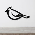 Black metal cardinal wall art with a bold silhouette design, mounted on a white wall above a light wood surface.