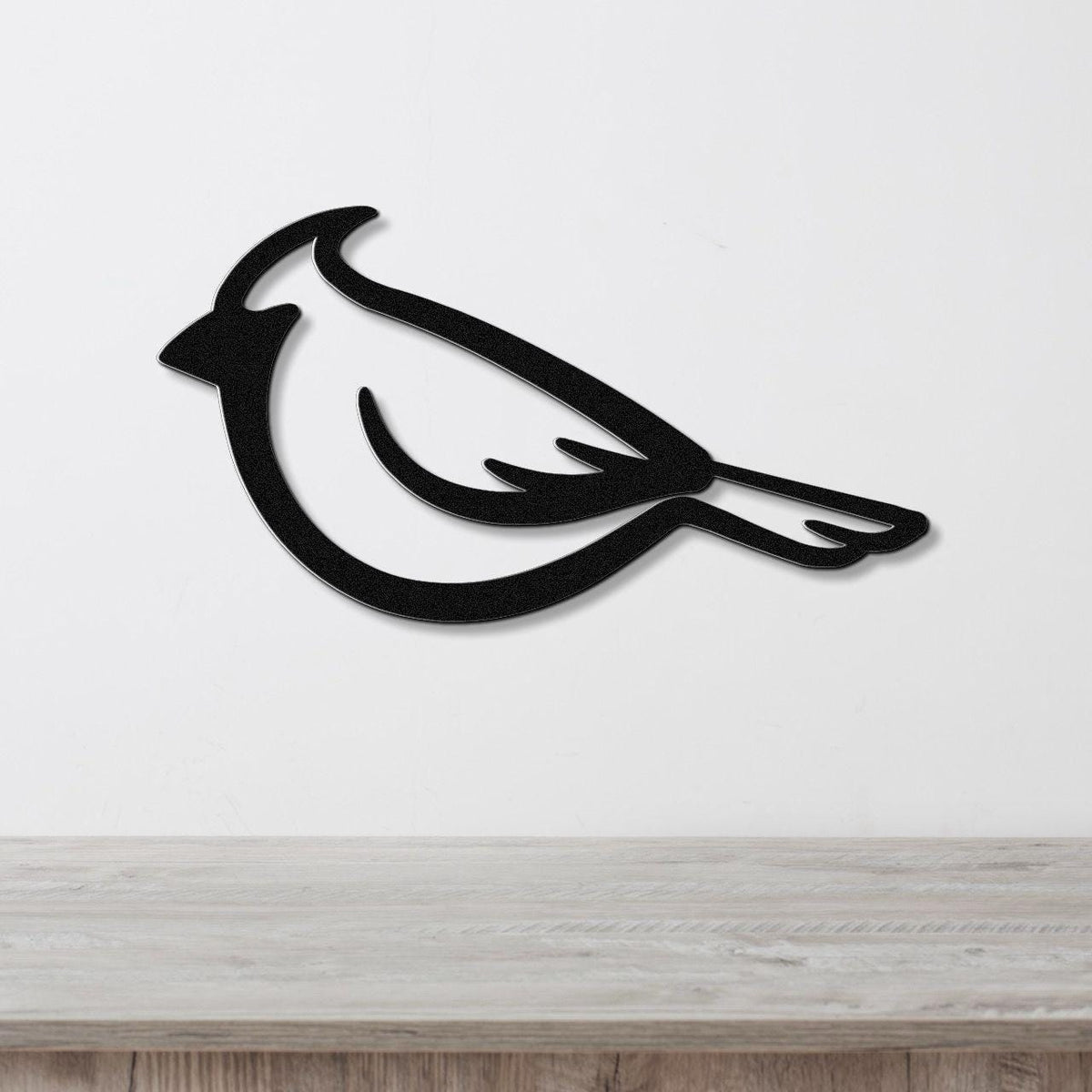 Black metal cardinal wall art with a bold silhouette design, mounted on a white wall above a light wood surface.