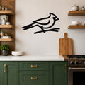 Black metal cardinal wall art in a minimalist silhouette style, perched on a branch, mounted on a tiled kitchen wall above a counter.