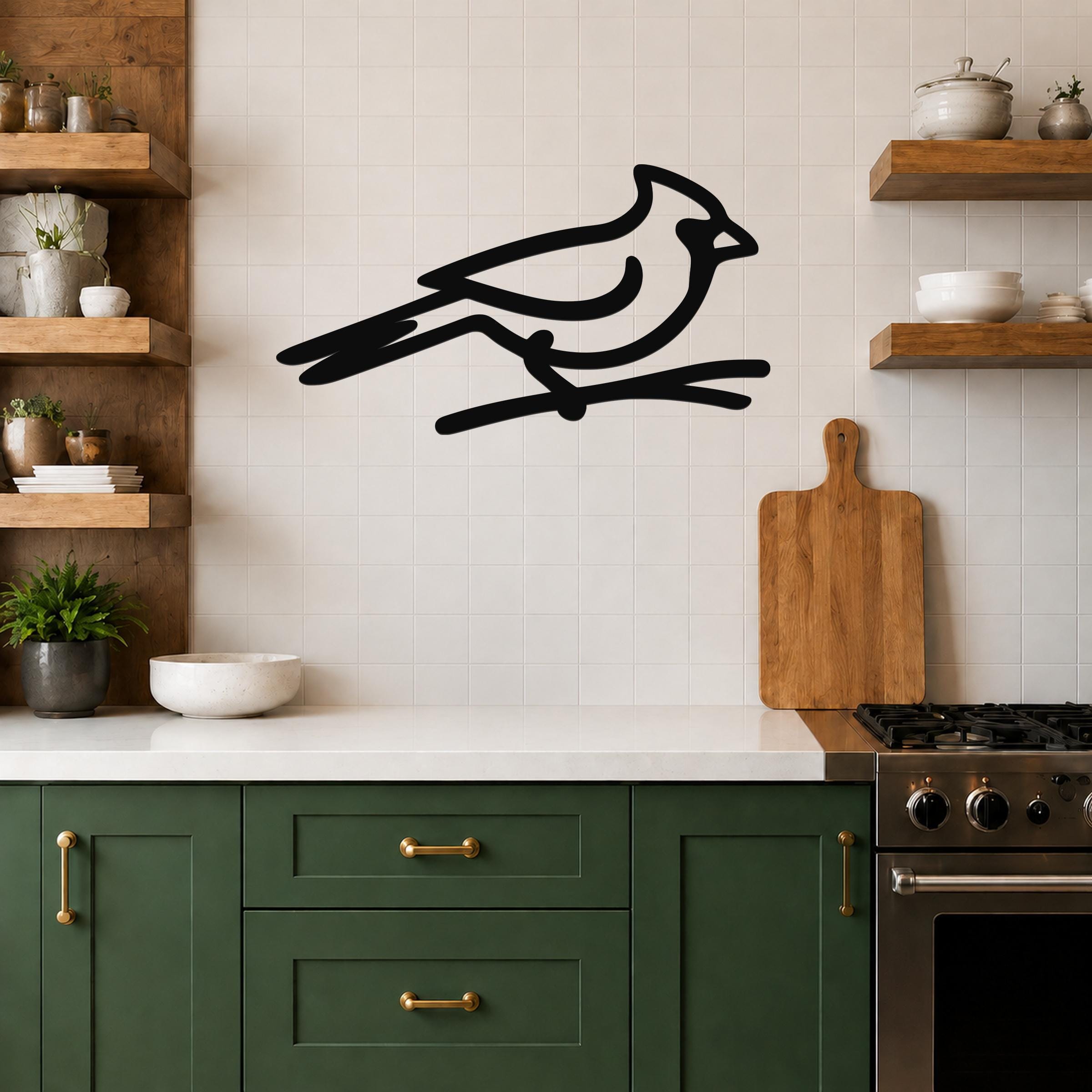 Black metal cardinal wall art in a minimalist silhouette style, perched on a branch, mounted on a tiled kitchen wall above a counter.