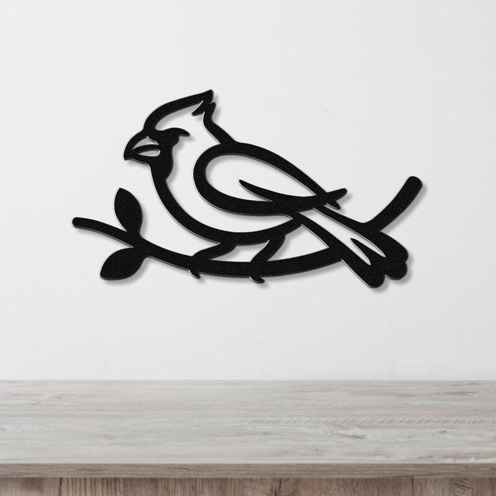 Black metal cardinal wall art with a branch silhouette, mounted on a white wall above a light wood counter.