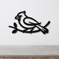 Black metal cardinal wall art with a branch silhouette, mounted on a white wall above a light wood counter.