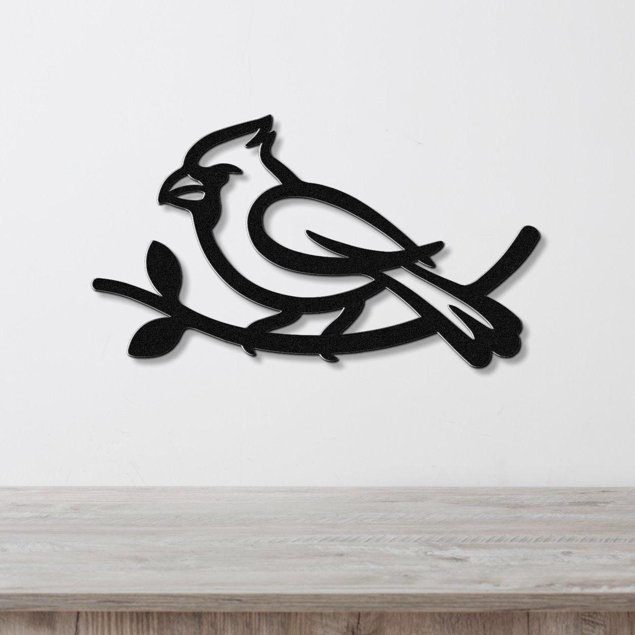 Black metal cardinal wall art with a branch silhouette, mounted on a white wall above a light wood counter.