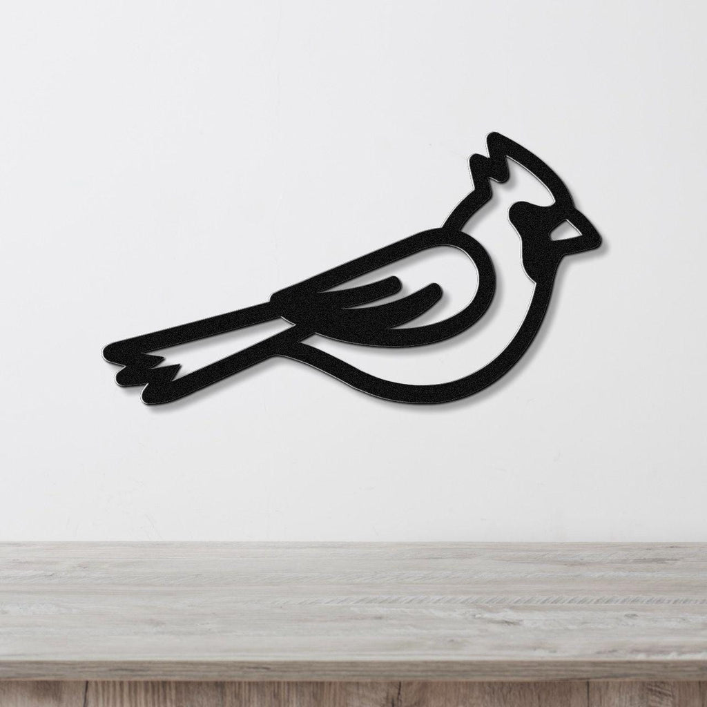 Black metal cardinal wall art with a minimalist silhouette design, mounted on a white wall above a light wood surface.