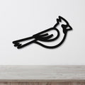 Black metal cardinal wall art with a minimalist silhouette design, mounted on a white wall above a light wood surface.